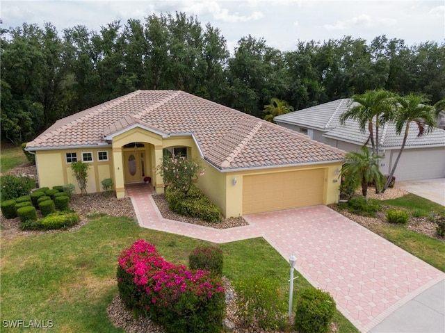 mediterranean / spanish-style home featuring an attached garage, driveway, stucco siding, a front yard, and a tiled roof