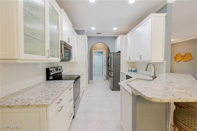kitchen featuring a peninsula, stainless steel appliances, ornamental molding, and arched walkways