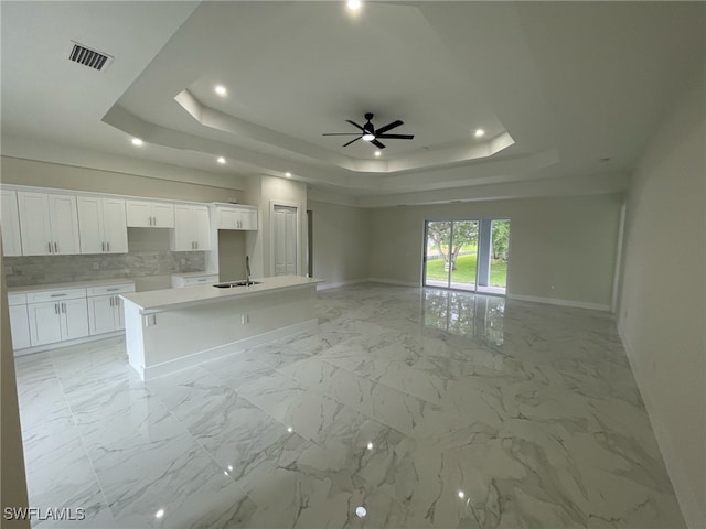 unfurnished living room with baseboards, a raised ceiling, ceiling fan, marble finish floor, and a sink
