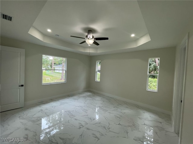 empty room with a tray ceiling, baseboards, and visible vents