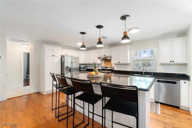 kitchen featuring dark countertops, appliances with stainless steel finishes, a sink, a breakfast bar area, and under cabinet range hood