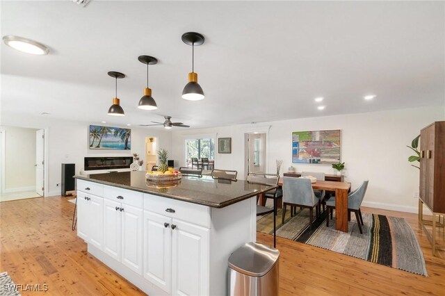 kitchen featuring a kitchen island, decorative light fixtures, dark countertops, light wood-type flooring, and white cabinetry