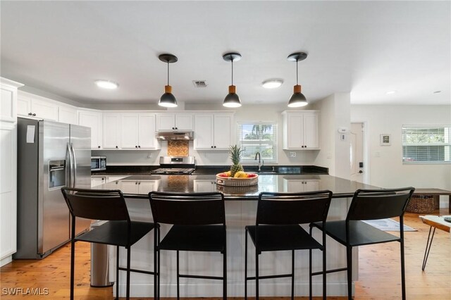 kitchen featuring white cabinets, dark countertops, stainless steel appliances, under cabinet range hood, and visible vents