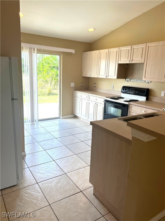 kitchen featuring light countertops, electric range, freestanding refrigerator, light tile patterned flooring, and lofted ceiling