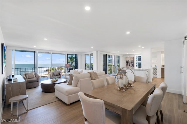 dining area with baseboards, a water view, a wall of windows, light wood-type flooring, and recessed lighting