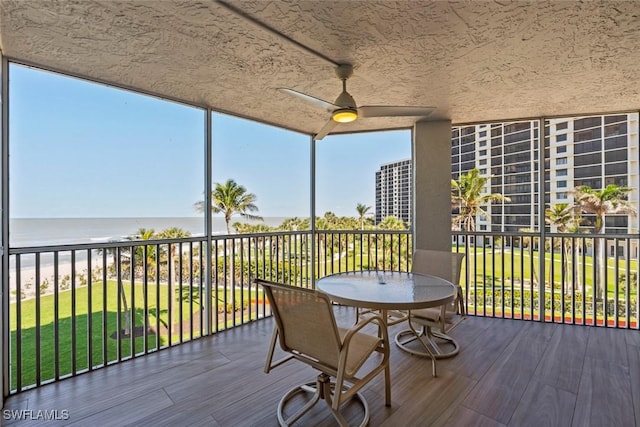 wooden terrace with ceiling fan, a water view, and a lawn