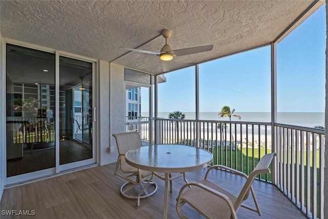 sunroom / solarium with a water view, wood finished floors, a ceiling fan, and a wall of windows