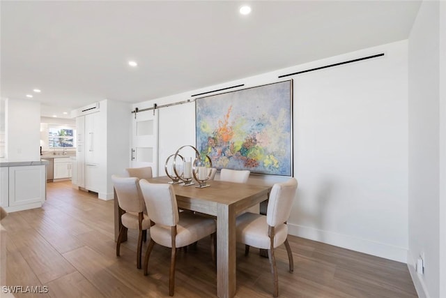 dining room with light wood-style flooring, recessed lighting, a barn door, and baseboards