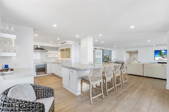 kitchen with wall chimney range hood, white cabinets, open shelves, and stainless steel oven