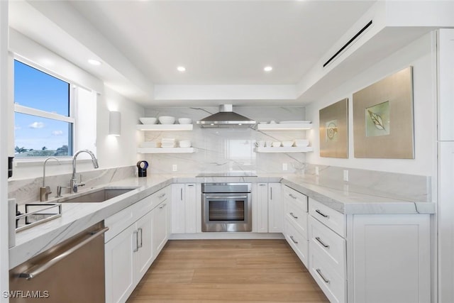 kitchen with a sink, wall chimney range hood, open shelves, and stainless steel appliances