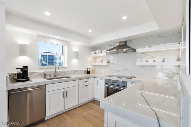 kitchen featuring open shelves, wall chimney exhaust hood, a sink, appliances with stainless steel finishes, and light stone counters