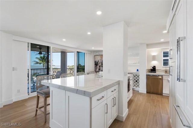 kitchen featuring light wood finished floors, stainless steel dishwasher, white cabinets, and a kitchen breakfast bar