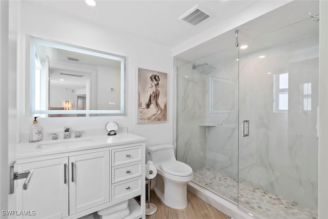 bathroom featuring vanity, visible vents, toilet, wood finished floors, and a marble finish shower