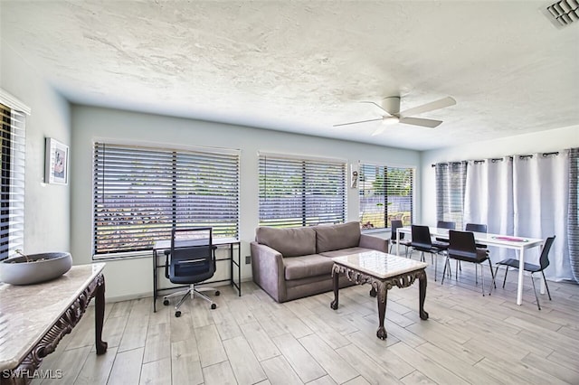 living area featuring light wood finished floors, visible vents, a textured ceiling, and ceiling fan