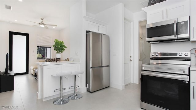 2343 Oil Well Rd, Naples, FL 34120 - kitchen with visible vents, white cabinets, ceiling fan, a kitchen breakfast bar, and stainless steel appliances