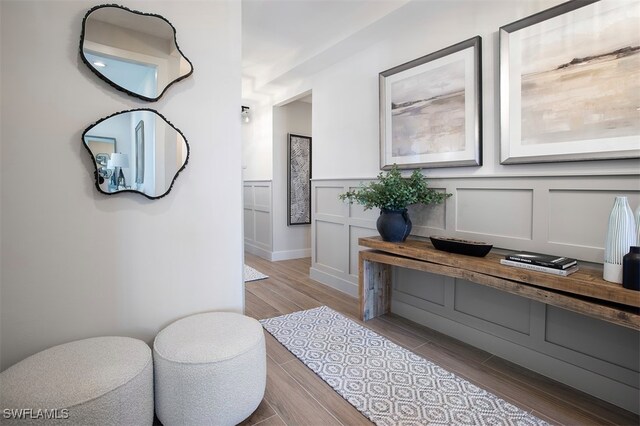 hall with a wainscoted wall, a decorative wall, and wood finished floors