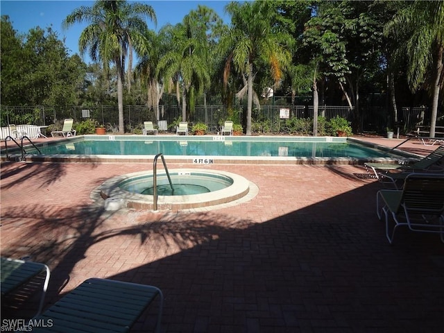pool with a patio, fence, and a hot tub