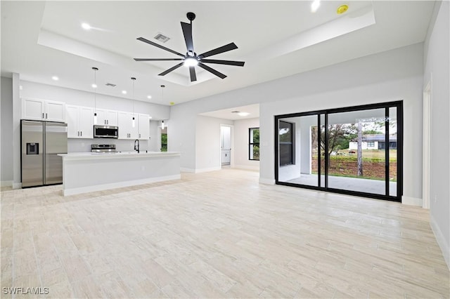 unfurnished living room featuring ceiling fan, a sink, visible vents, and a raised ceiling