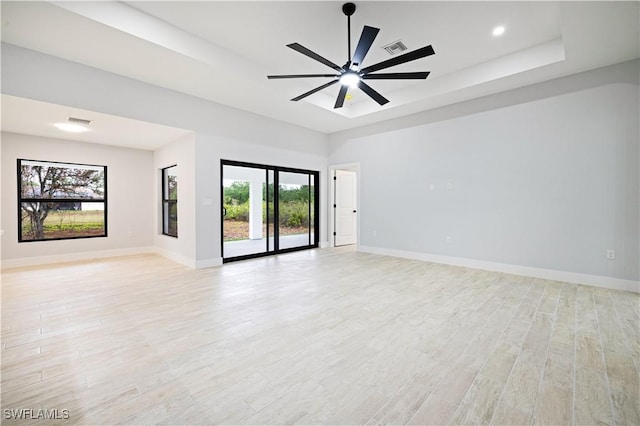 empty room with baseboards, visible vents, light wood-style floors, and a raised ceiling