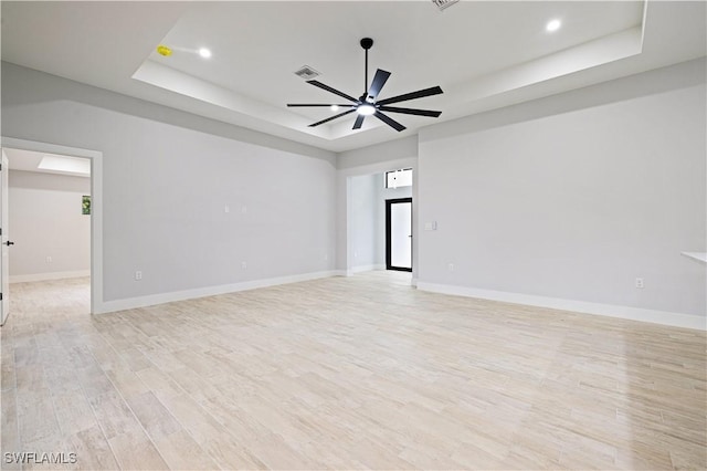 unfurnished room with a ceiling fan, light wood-style floors, a tray ceiling, baseboards, and visible vents