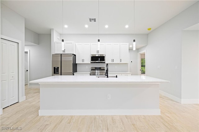 kitchen with a sink, an island with sink, stainless steel appliances, light countertops, and visible vents