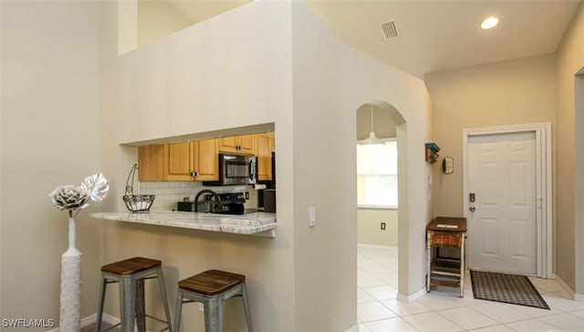 6645 Huntington Lakes Cir Unit 201, Naples, FL 34119 - kitchen featuring a kitchen breakfast bar, light countertops, visible vents, arched walkways, and tasteful backsplash