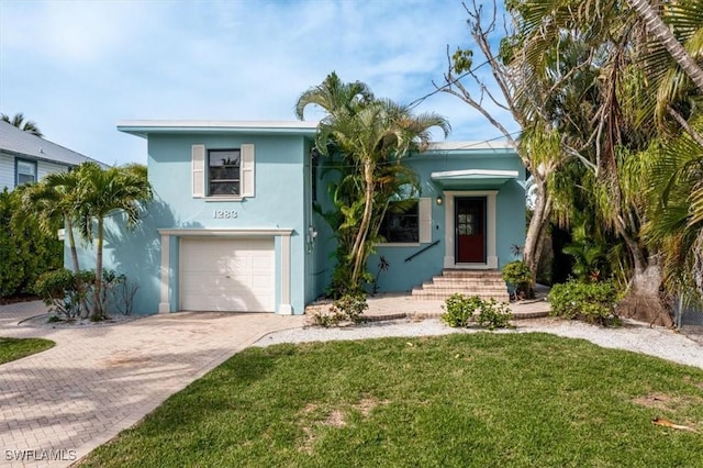 view of front of property featuring a garage, a front yard, stucco siding, and decorative driveway