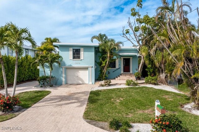 tri-level home featuring a garage, a front yard, stucco siding, and decorative driveway
