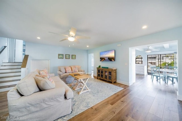 living room featuring ceiling fan, stairway, wood finished floors, and baseboards