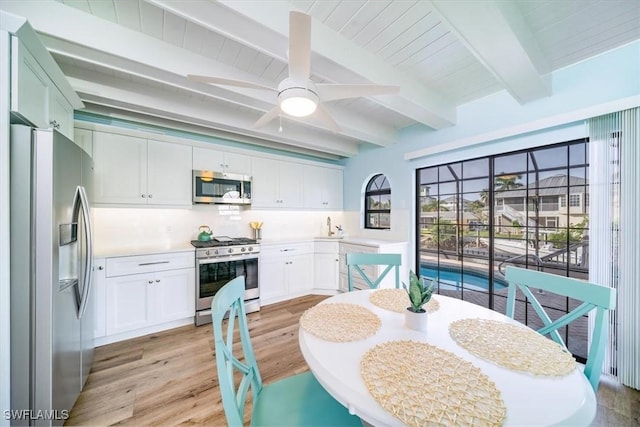 kitchen featuring white cabinetry, backsplash, light wood-style floors, beamed ceiling, and appliances with stainless steel finishes