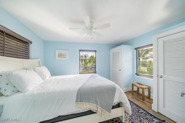 bedroom featuring baseboards, multiple closets, a ceiling fan, and wood finished floors