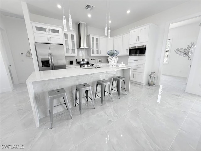 kitchen featuring a large island, wall chimney range hood, white cabinets, visible vents, and stainless steel appliances