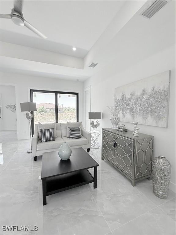 living room featuring visible vents, a raised ceiling, marble finish floor, and a ceiling fan