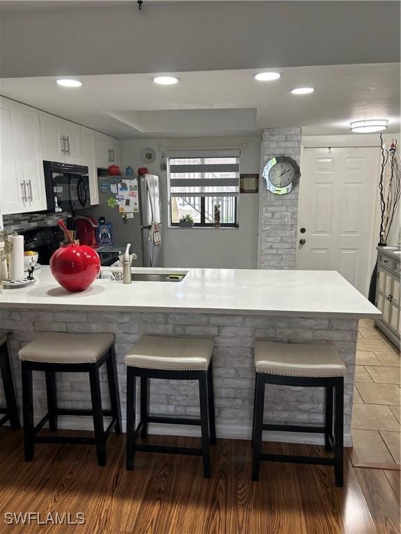 kitchen featuring black microwave, a peninsula, white cabinetry, freestanding refrigerator, and a kitchen bar
