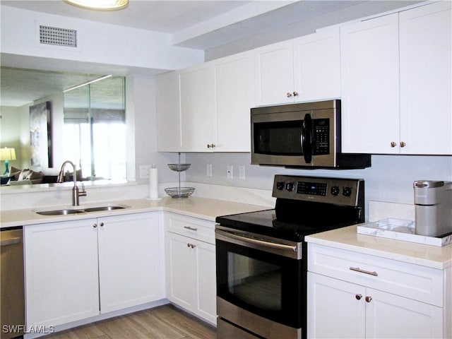 kitchen with white cabinets, stainless steel appliances, light countertops, visible vents, and a sink