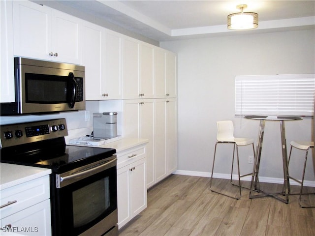 kitchen with white cabinets, baseboards, light wood-style floors, light countertops, and appliances with stainless steel finishes
