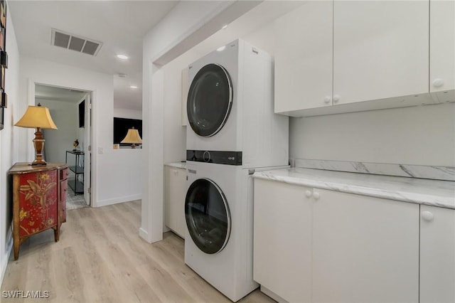 laundry area with light wood-type flooring, cabinet space, stacked washer and dryer, visible vents, and recessed lighting