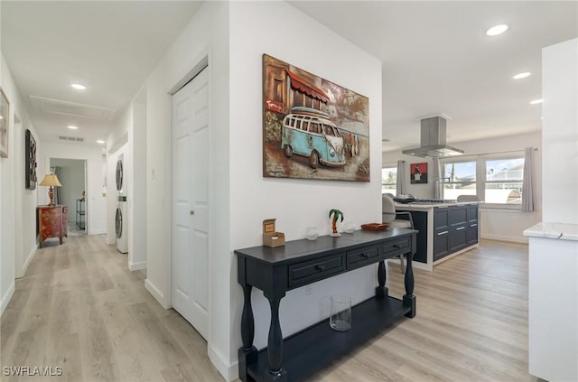 corridor with attic access, visible vents, stacked washer / dryer, and light wood finished floors