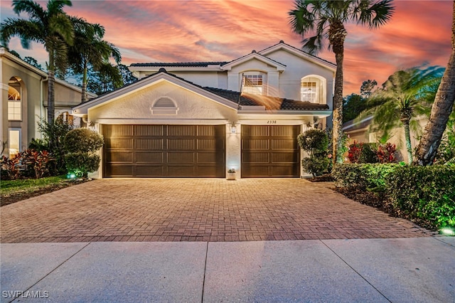 mediterranean / spanish-style home featuring an attached garage, decorative driveway, stucco siding, and a tiled roof