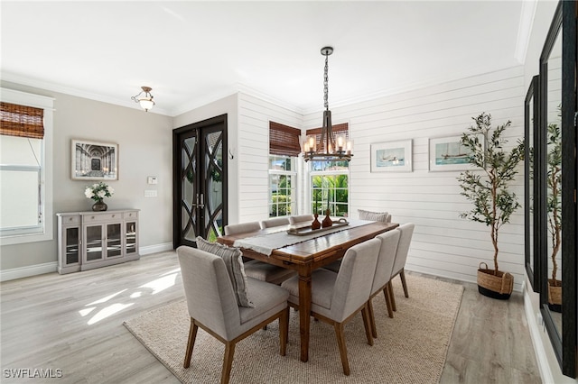 dining space featuring crown molding, light wood-style floors, a chandelier, wood walls, and baseboards