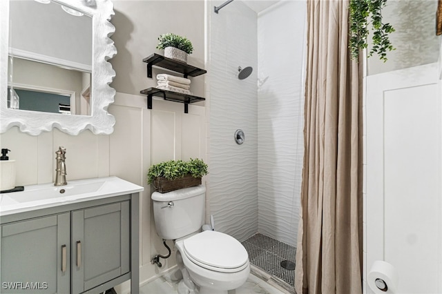 full bathroom featuring wainscoting, a shower stall, vanity, toilet, and a decorative wall