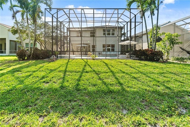 rear view of house featuring a lawn, glass enclosure, and stucco siding