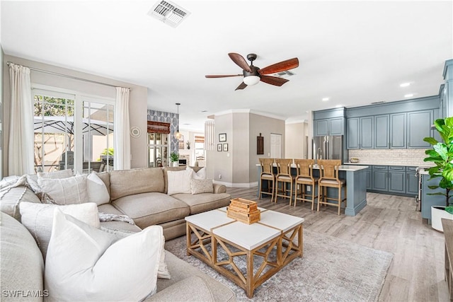 living area featuring ceiling fan, visible vents, crown molding, baseboards, and light wood finished floors