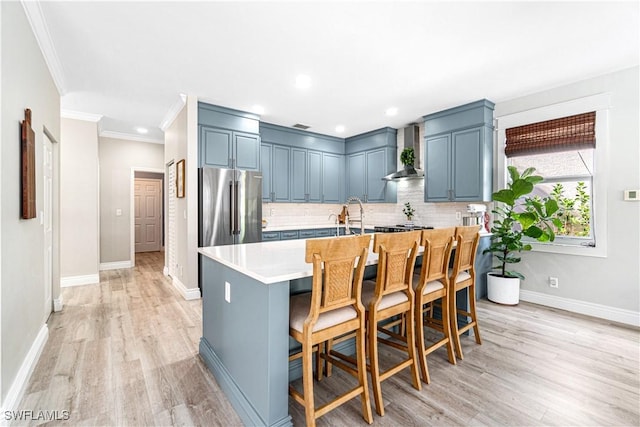kitchen featuring light wood finished floors, light countertops, wall chimney exhaust hood, high end refrigerator, and backsplash