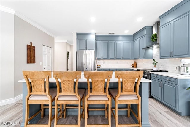 kitchen with wall chimney range hood, appliances with stainless steel finishes, a center island, decorative backsplash, and light wood-type flooring