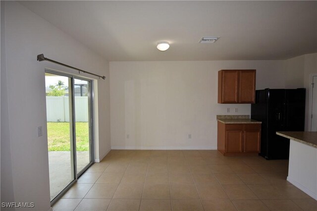 kitchen with baseboards, light tile patterned floors, black fridge, visible vents, and brown cabinetry