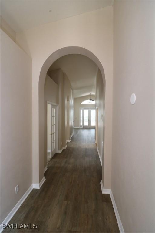 hallway featuring arched walkways, dark wood-type flooring, french doors, and baseboards