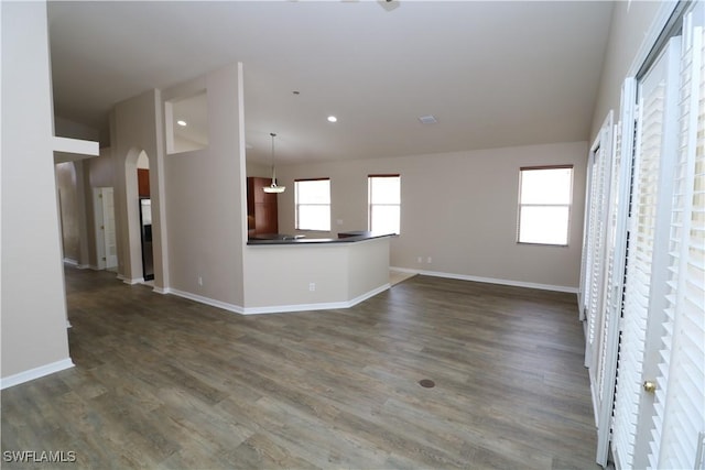 unfurnished living room featuring dark wood-style flooring, baseboards, recessed lighting, and arched walkways