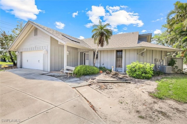 ranch-style home with concrete driveway, central AC, board and batten siding, and an attached garage