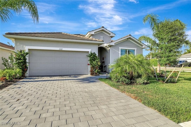 single story home featuring an attached garage, stucco siding, a front lawn, and decorative driveway